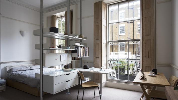 Floor to ceiling compressed modern open wardrobe shelving and room divider in small apartment. Modular shelving system.